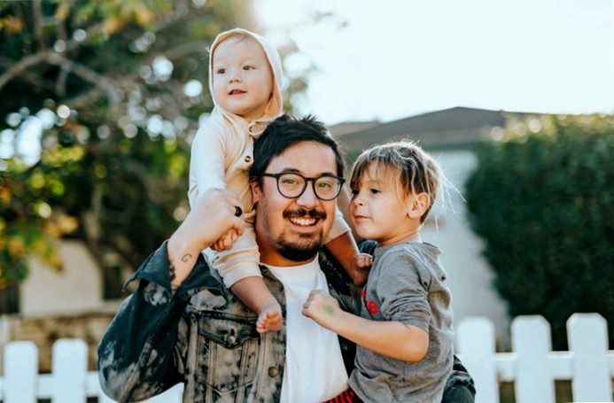 father holding two kids in front of his new home, after receiving a gift letter to help fund his down payment